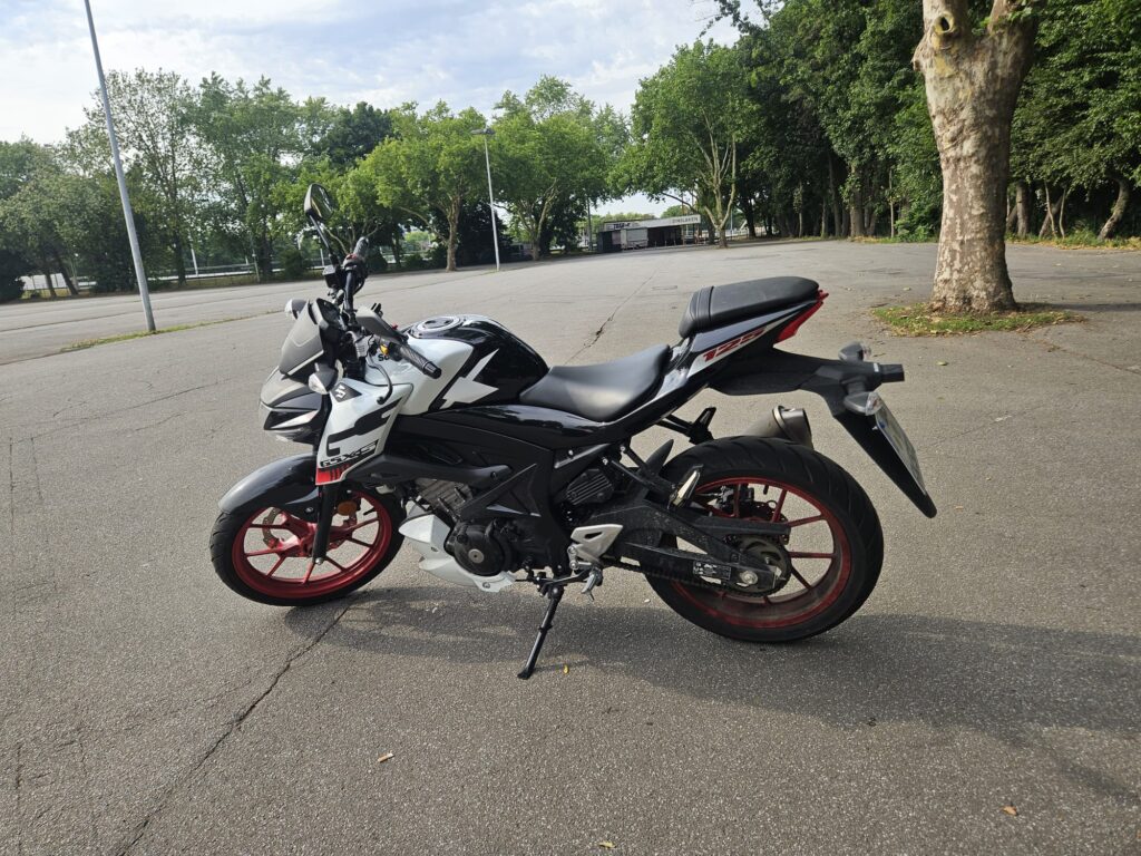 Ein weißes Motorrad mit roten Felgen auf leerem Parkplatz.