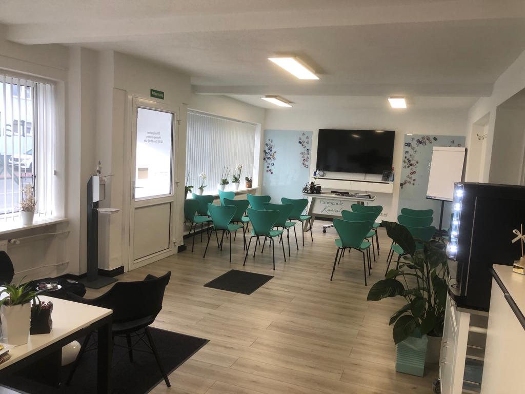 Ein heller Besprechungsraum mit türkisfarbenen Stühlen und einem großen Bildschirm an der Wand.