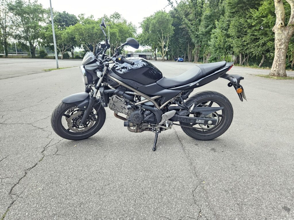 Schwarzes Motorrad geparkt auf leerem Asphalt, umgeben von grünen Bäumen.