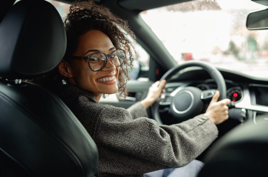 Lächelnde Managerin, die Auto fährt und beide Hände am Lenkrad hält, auf dem Weg zur Arbeit